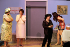 Four women talking, one in a short skirt, one in a long beige dress with her hands near her mouth, one in a floral print dress, and one in a
       dark pantsuit