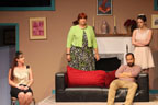 A woman in a gold lame top tied up in a chair, a man sitting on a couch, a woman wearing a green sweater, and a woman
       in a white dress