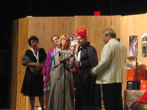 A woman in a black dress and mink stole, a woman in a sparkling purple coat, a blond woman, a woman in a brown raincoat, a man in a suit,
       black cloak and red turban, and a man in a white tuxedo jacket